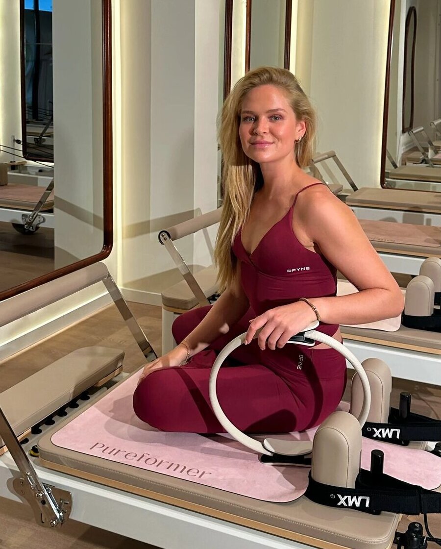 Oprichtster van Pureformer zit met een pilates ring op een reformer met de roze Pureformer mat in een lichte studio